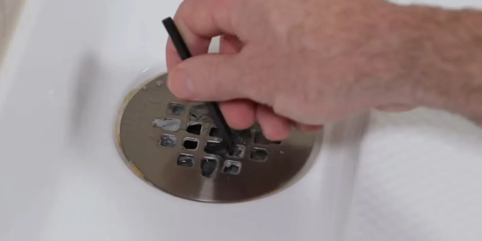 Plumber's hand feeding a drain auger cable into a floor drain