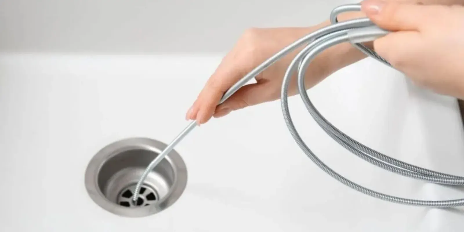Hand guiding a flexible drain snake into a white sink drain